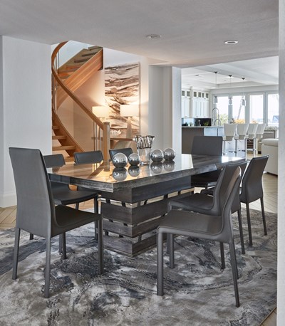 Image of a modern grey dining table with grey dining chairs on an abstract grey rug in front of staircase.