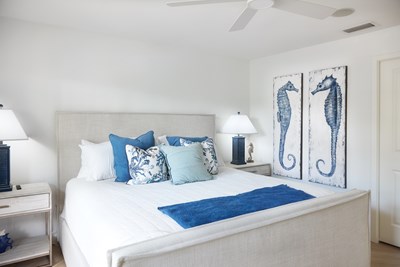 Image of a light grey upholstered bed with blue and white bedding, and seahorse art on the wall.
