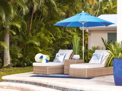 Two cushioned outdoor chaises with a blue sun unbrella on a Florida patio with lush palm trees.