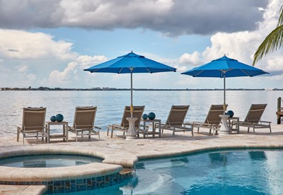 Image of a pool with six chaises facing the water and blue sun umbrellas.