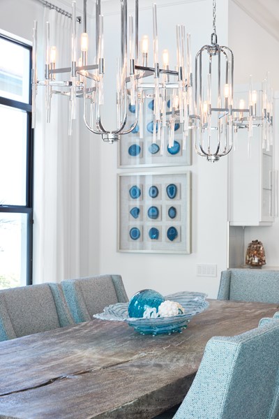 Live edge wooden dining table with ight blue chairs and chandeliers.
