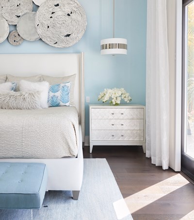 Blue & White bedroom with flowers on nightstand & silver discs hanging over headboard.