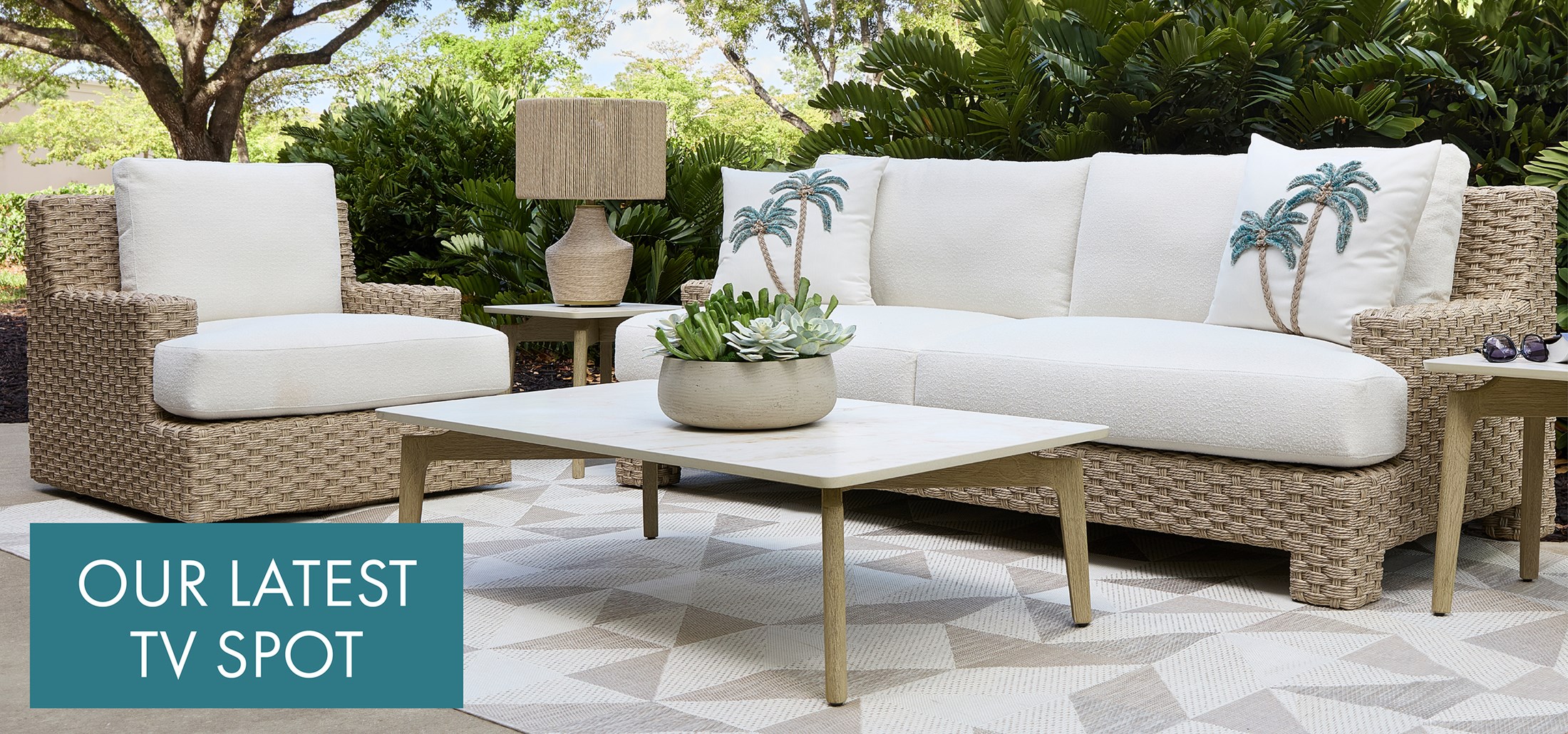 Image of the Trieste Outdoor Sofa and chair outdoors with cocktail and end tables. Text: Our Latest TV Spot. Links to TV Spot on Youtube.
