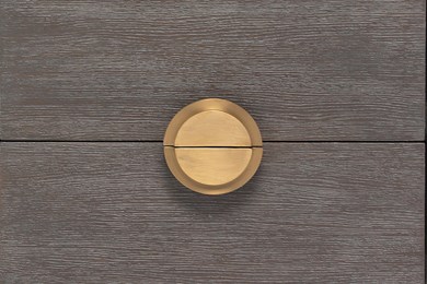 a photo of the front of a nightstand with focus on the wooden drawer fronts and brass drawer pull